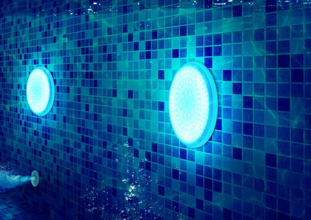 Underwater LED pool lights illuminating a tiled pool wall in blue.