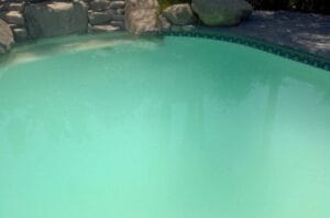 Swimming pool with cloudy water and high-pressure gauge indicating need for filter cleaning.