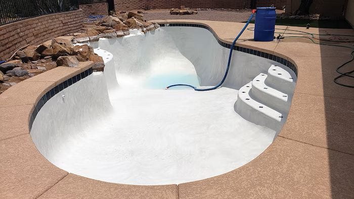 A clean pool with a newly applied plaster and a hose nearby.