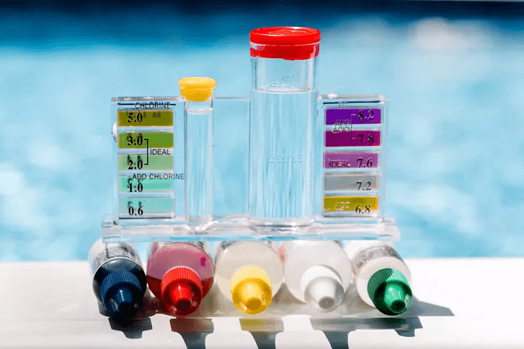 A pool water test kit featuring tools for measuring pH, with a sparkling pool visible in the background.